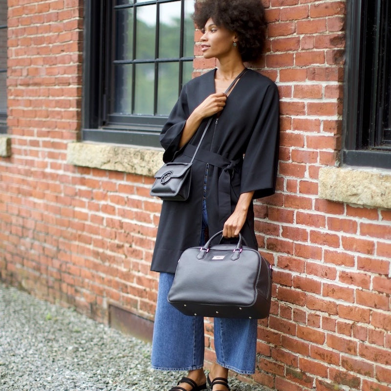 Woman leaning against wall holding Newport travel bag - Darby Scott