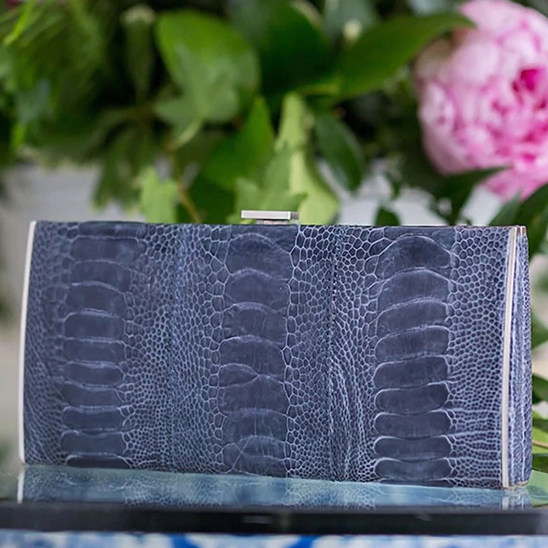 Denim blue Ostrich Leg Box Wallet in front of pink and green floral arrangement - Darby Scott