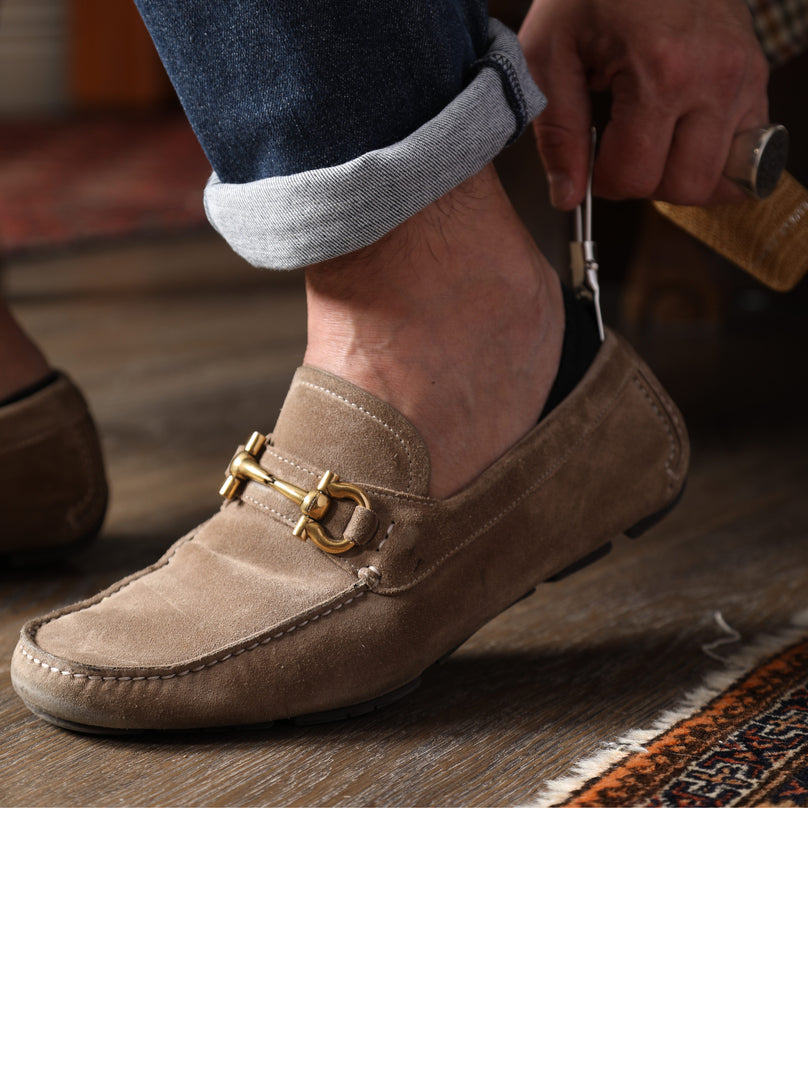 Man using shoehorn to put on brown suede shoes