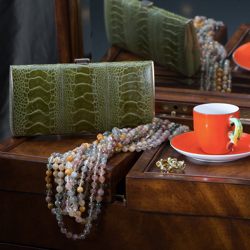 Olive green box wallet with necklace by designer Darby Scott next to tea cup on desk