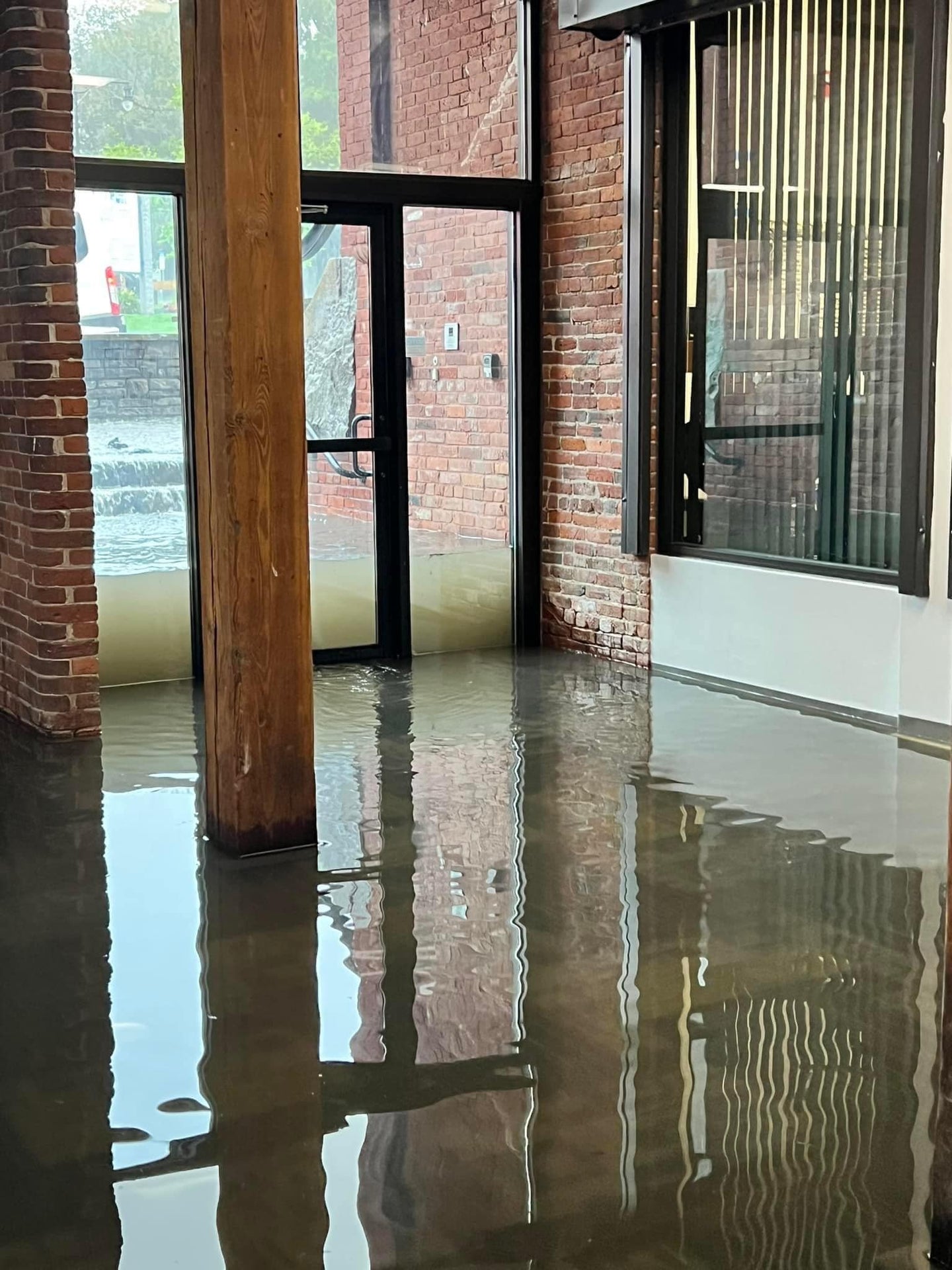 Flooded interior with water on the floor, brick walls, and large windows. at East Mill North Andover