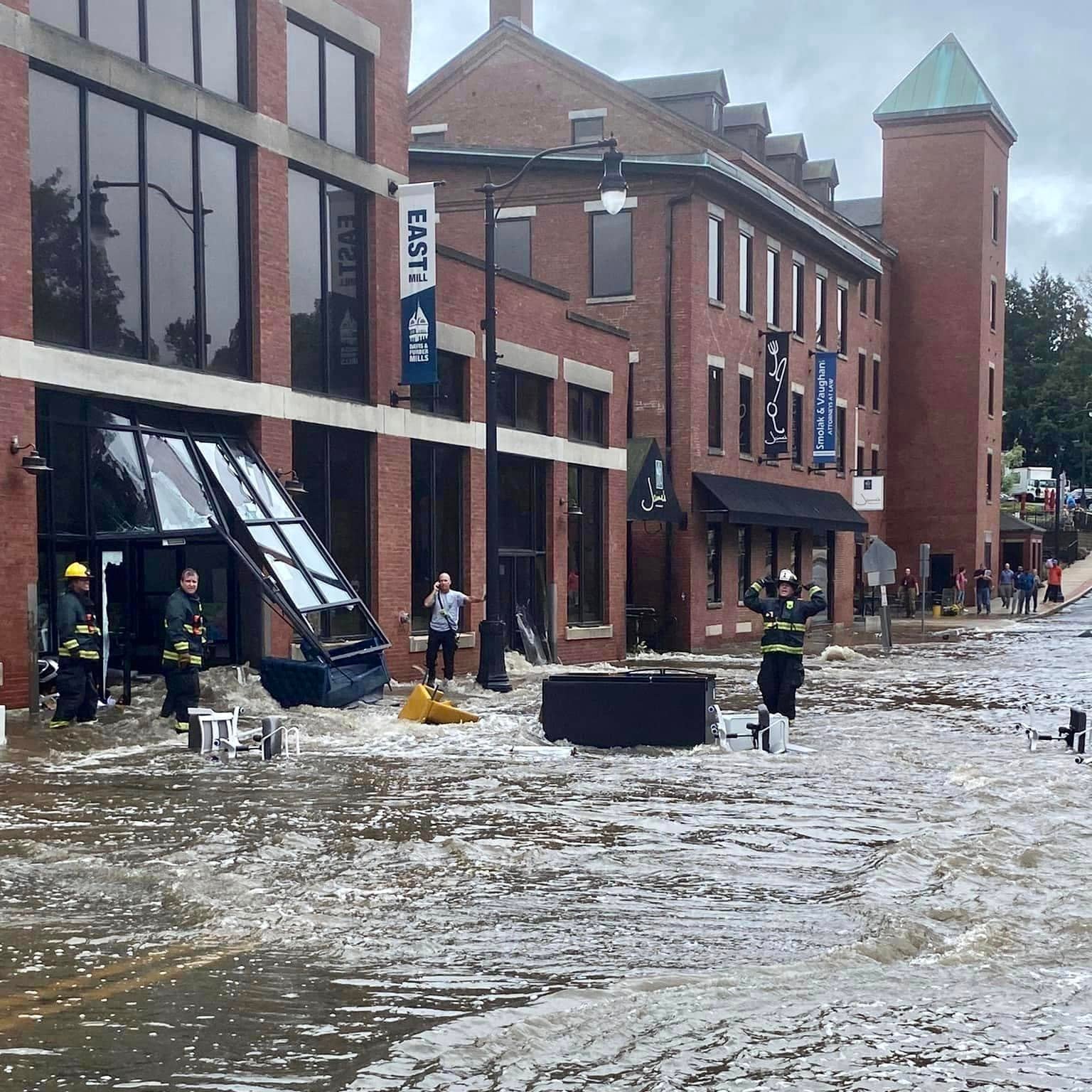 Flooded street with people and emergency vehicles in front of brick buildings where darby scott office was located.
