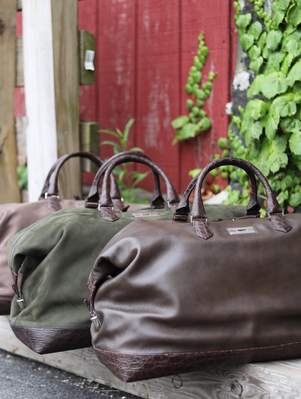 3 AspenTravel Duffle Bags on the ground next to a red door with green vines