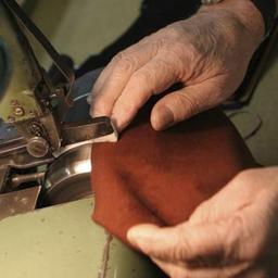 Workman's hands shown sewing leather 