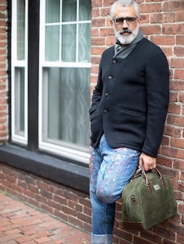 Man leaning against brick wall holding a Newport Carry-on Bag - Darby Scott