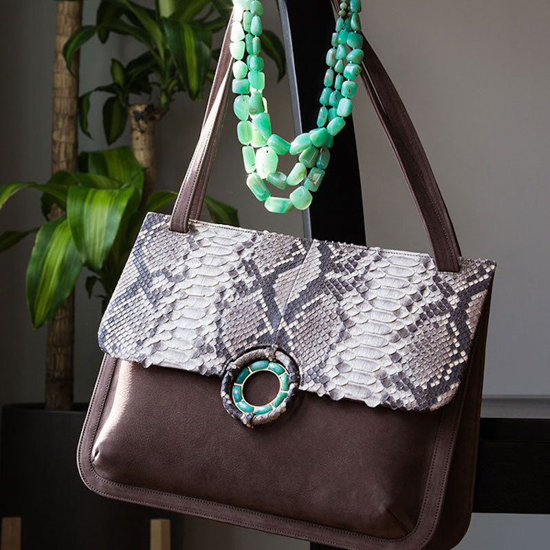 Suede and python bag with chrysoprase grommet detail and a multi-strand chrysoprase necklace hanging on a chair back