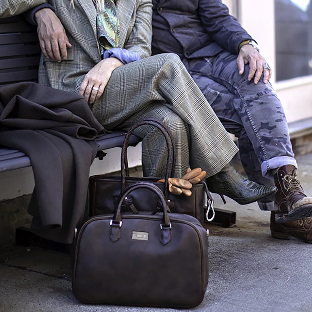 Newport Leather Travel Bag on ground in front of couple sitting on bench - Darby Scott