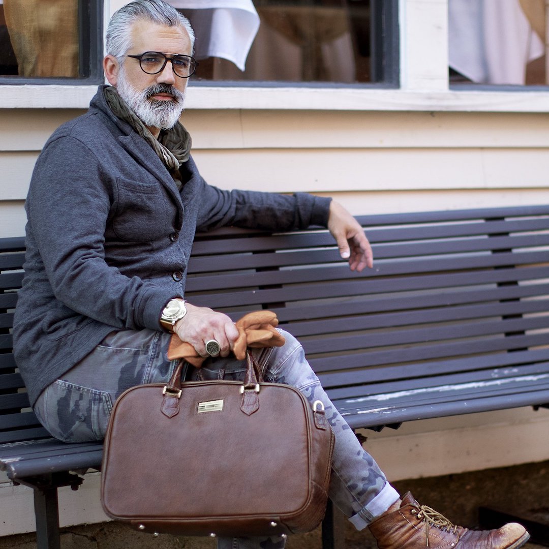 Man on bench holding a brown leather newport monogram carry-on bag