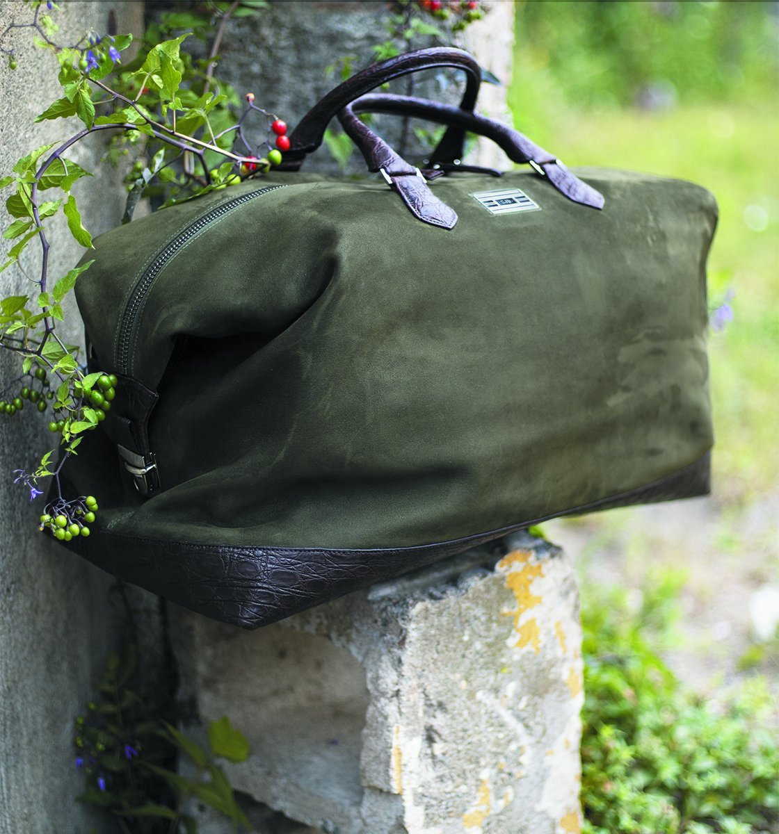 Green suede Aspen travel bag on a concrete pillar -Darby Scott