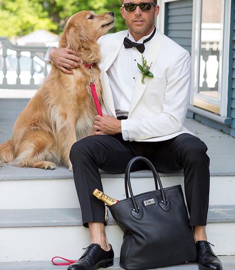 Man in white suit jacket with Essex tote and dog sitting on porch